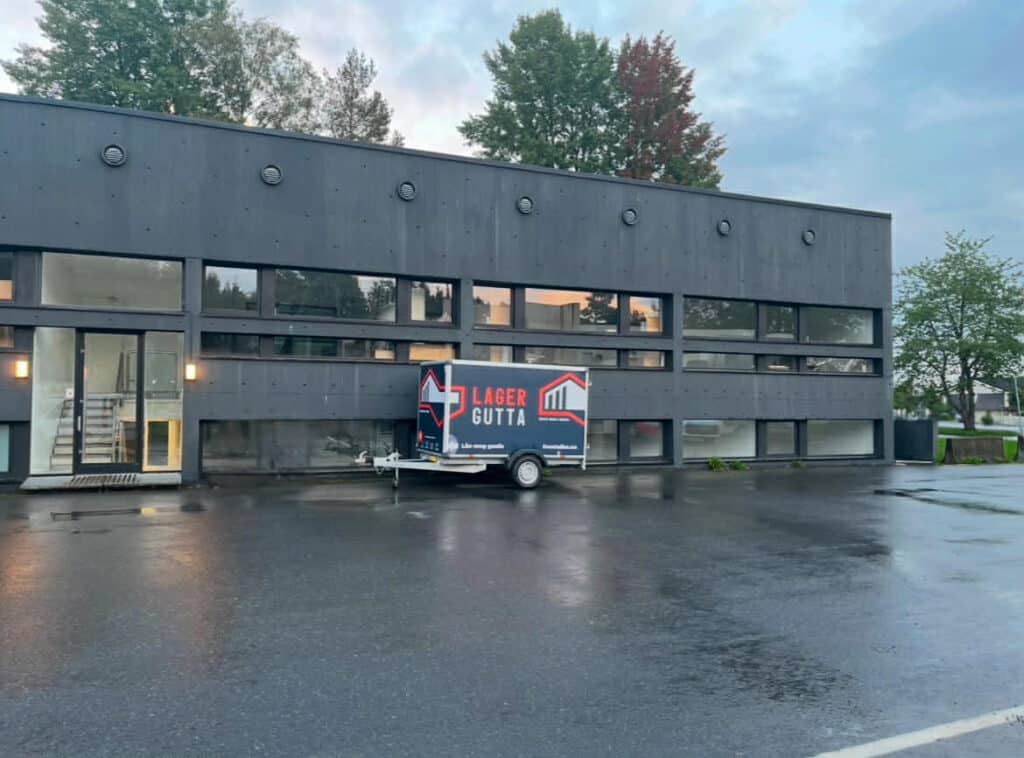 Lagergutta Freetrailer-tilhenger parkert utenfor mørk næringsbyggfasade.